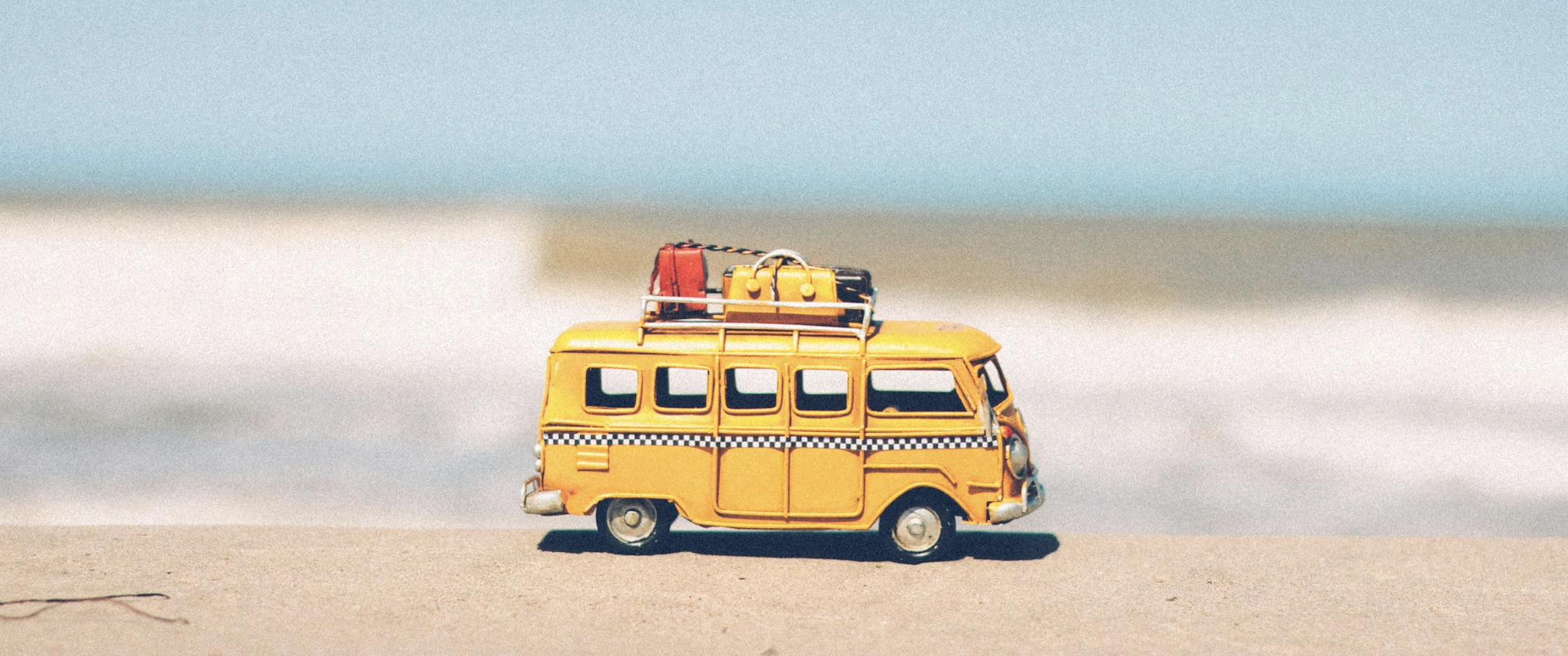 Mini van amarela de viagem com malas diante de um fundo colorido